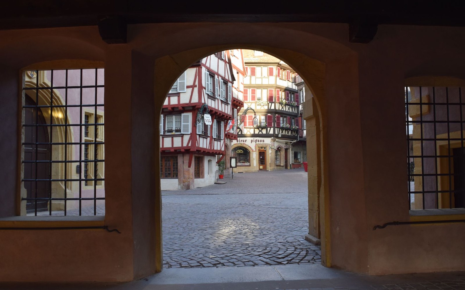 Archway framing a cobblestone square lined with half-timbered Alsatian houses