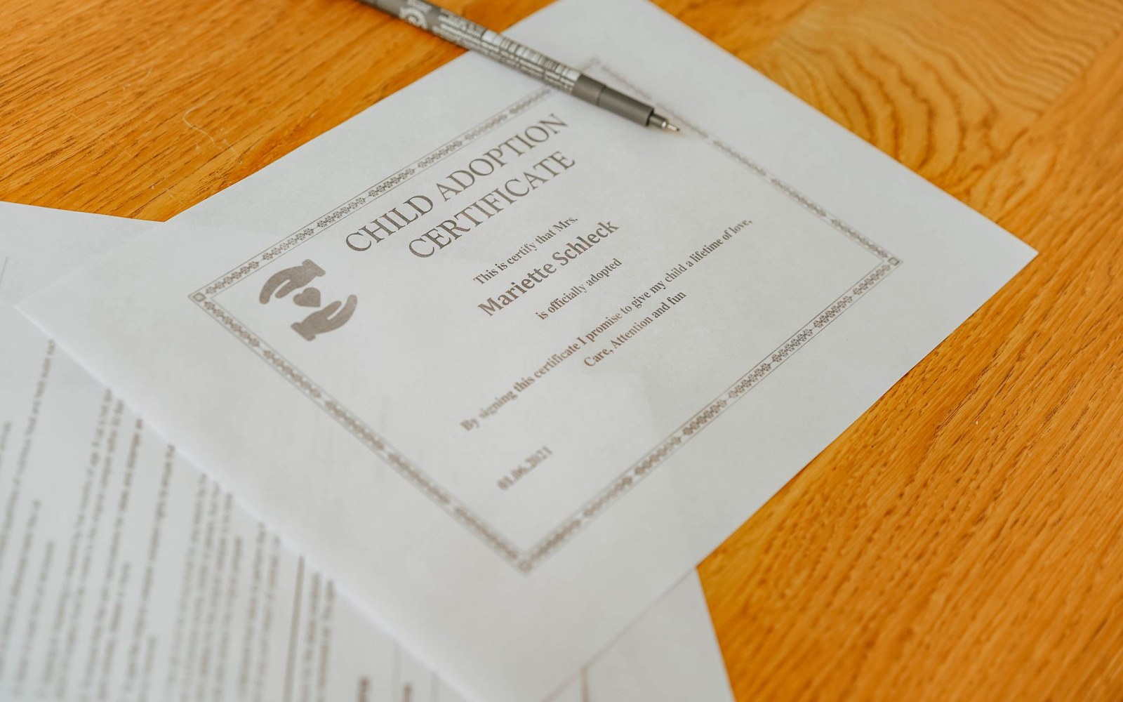 A printed child adoption certificate lies on a wooden table beside a pen