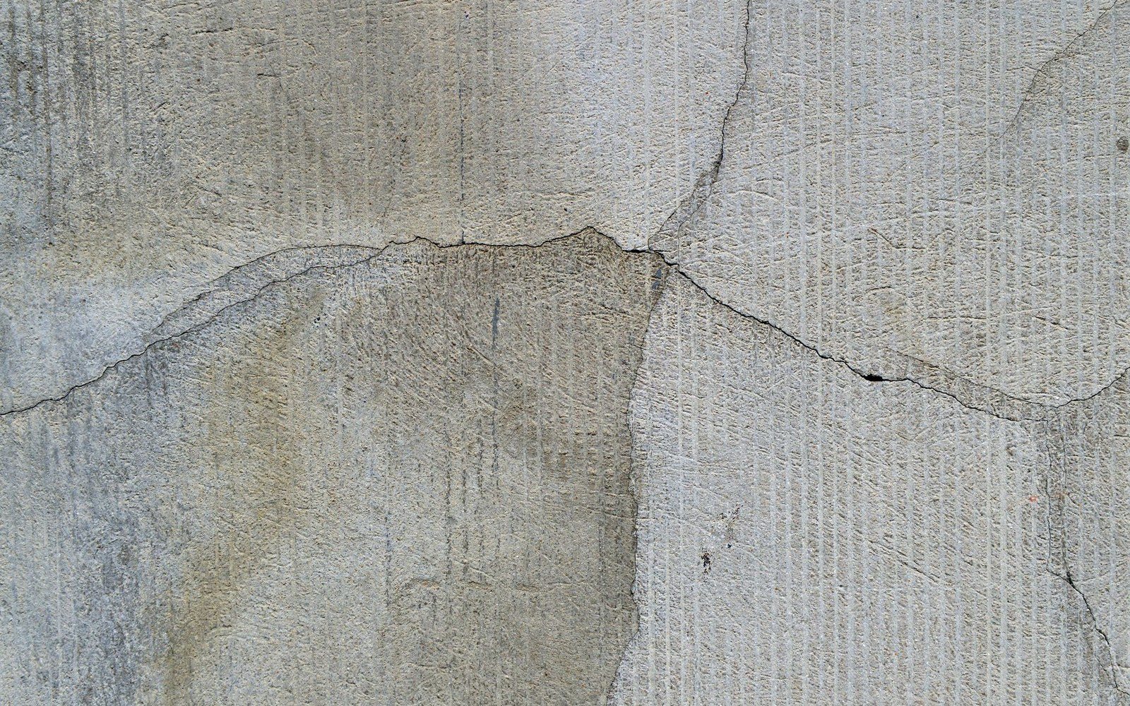 Cracked cement render on a wall showing vertical tool marks and staining
