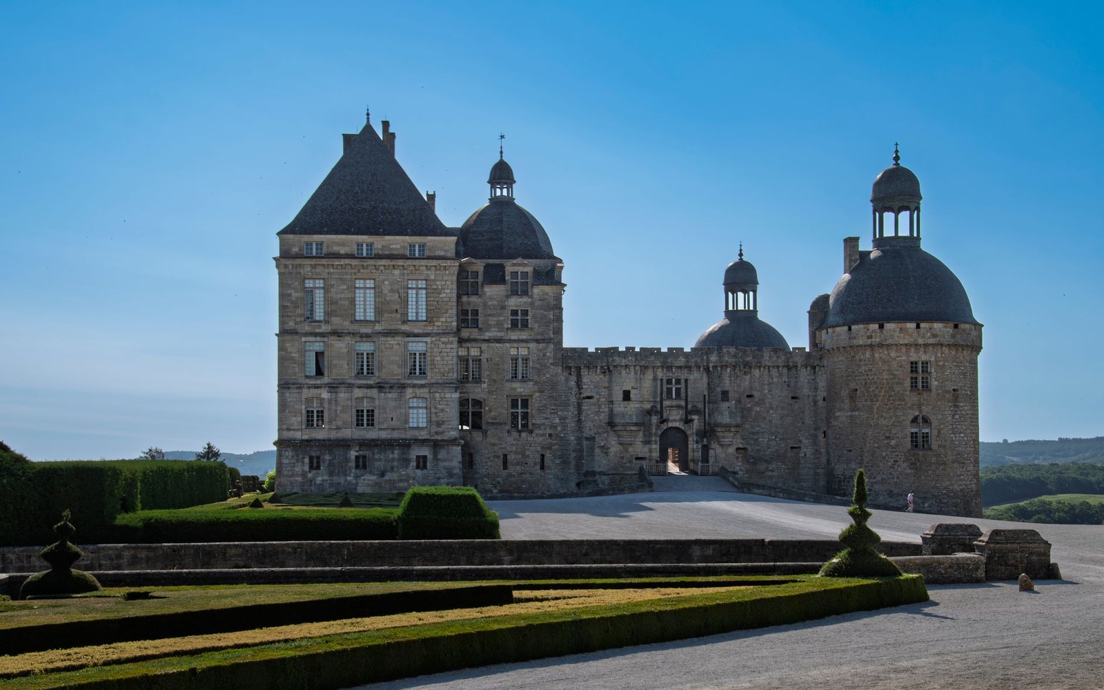 Stone château with round turrets and a central tower, fronted by manicured lawns