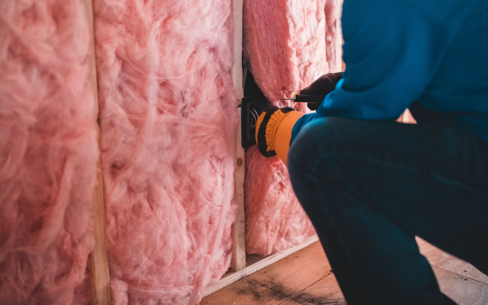 Worker installs pink fiberglass batt insulation between wall studs in an unfinished room