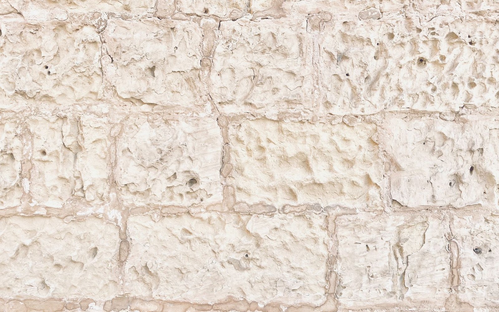 Rows of pale, weathered tuffeau stone blocks with rough textured surfaces and mortar joints