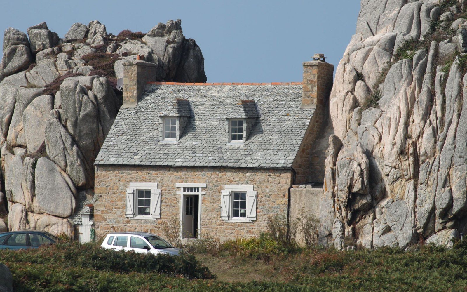 The granite end wall of a Breton longère, blind north elevation, late-afternoon light raking the joint lines